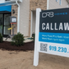 Sales office of a new home community with a large sign displaying visiting hours and contact information.