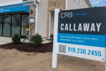 Sales office of a new home community with a large sign displaying visiting hours and contact information.