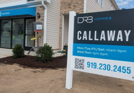 Sales office of a new home community with a large sign displaying visiting hours and contact information.